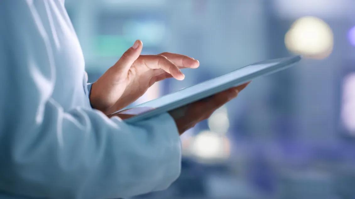 Person in a white lab coat using a tablet