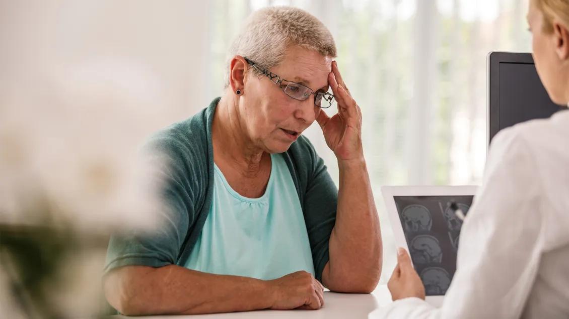 woman touching head talking to front desk person