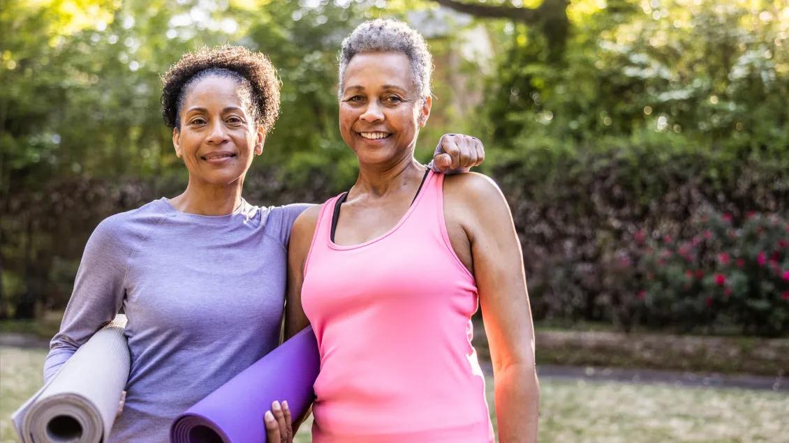two women holding yoga mats and posing for a photo