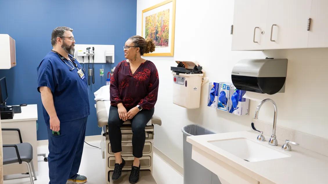 Photo of a male RN speaking with a female patient in a Michigan Clinical Research Unit exam room