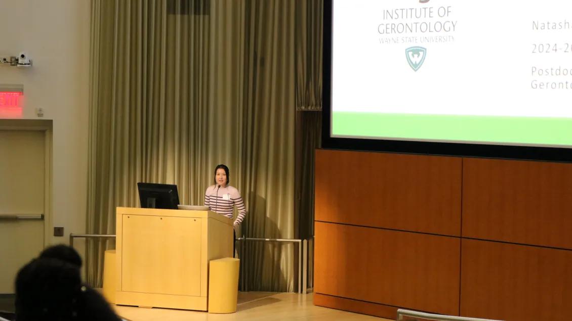 a woman in a purple striped shirt presenting in front of a screen 