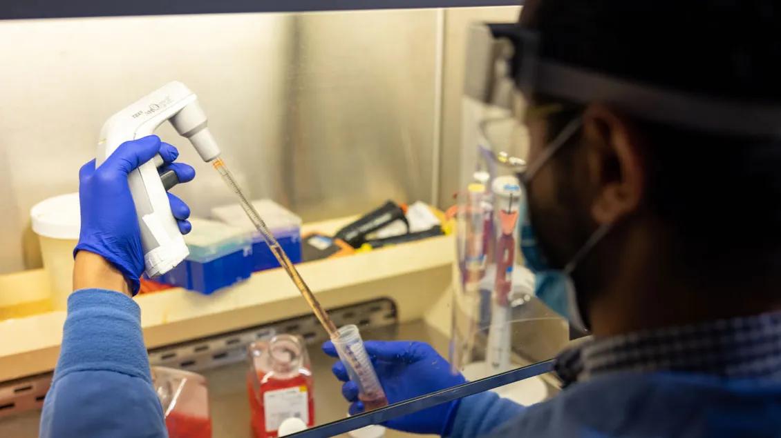 Looking over the shoulder of a male lab technician using a pipette