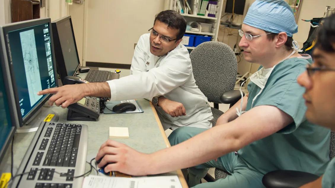 One doctor points at screen as two colleagues study the displayed MRI scans