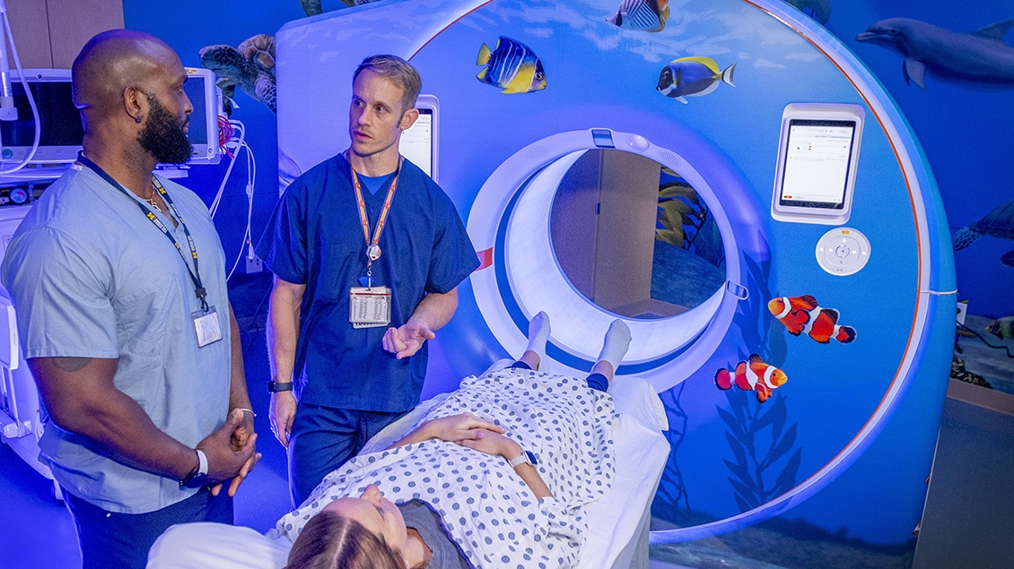 Patient positioned in front of MRI scanner as two doctors converse nearby