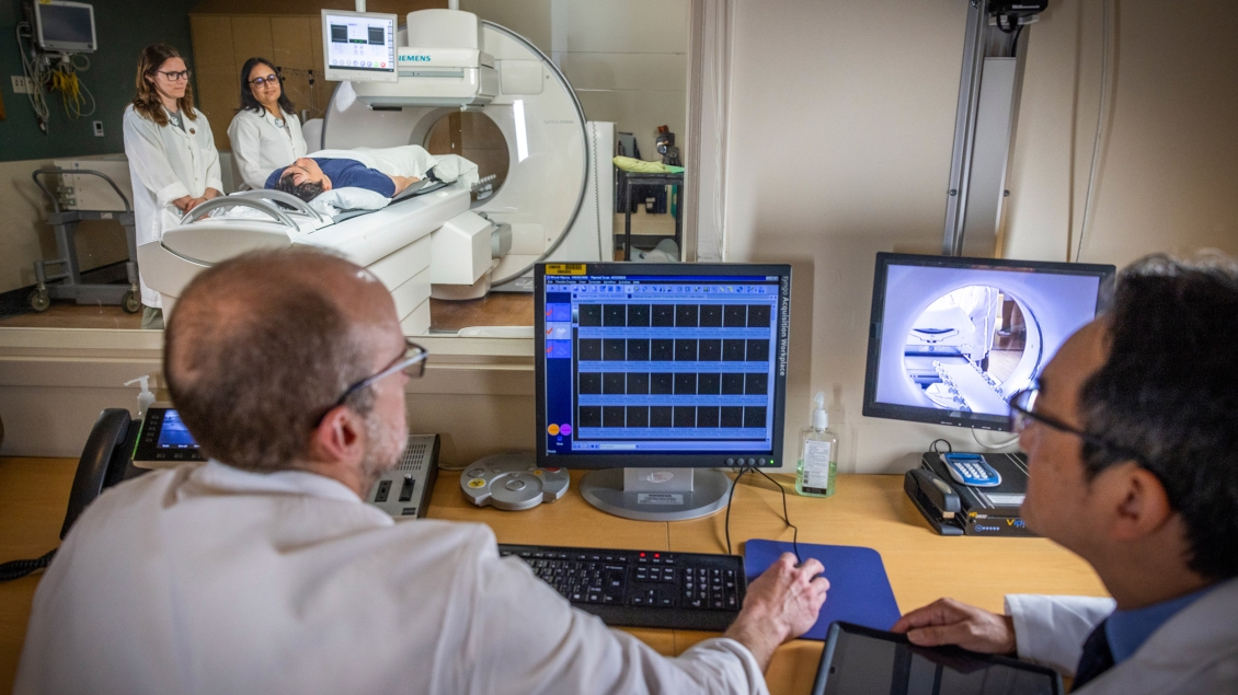 While two clinicians study MRI images, another pair engages with a patient nearby