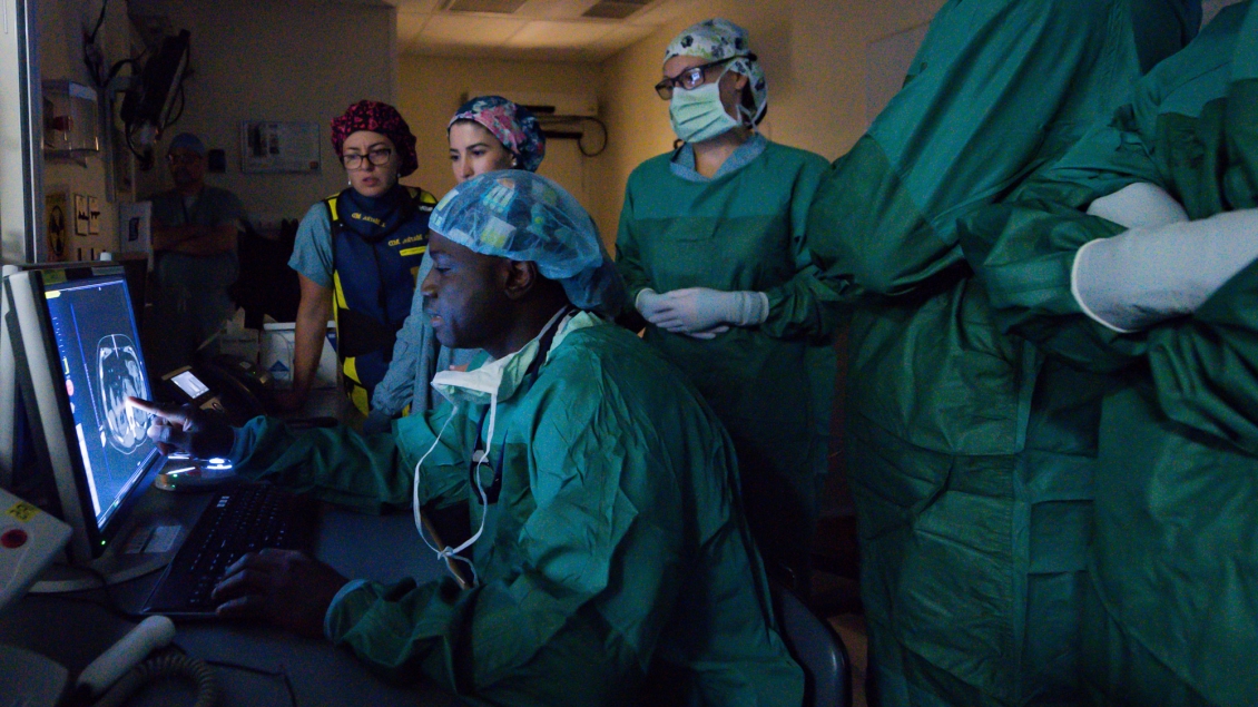 Medical team of six evaluating MRI scans on monitor