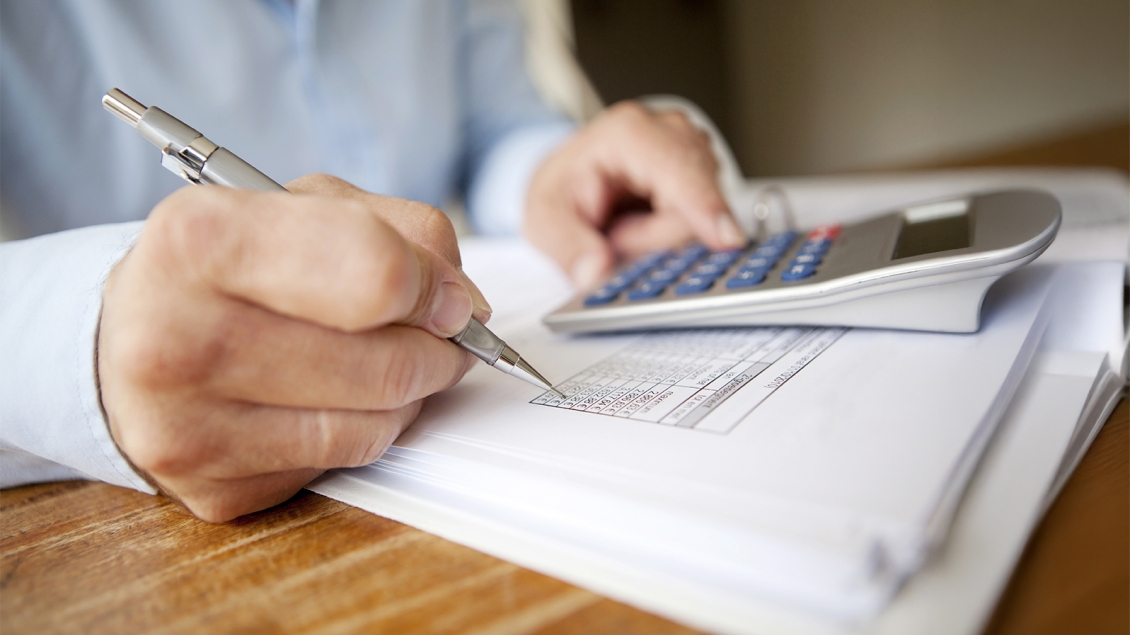 close-up of person writing notes and using a calculator