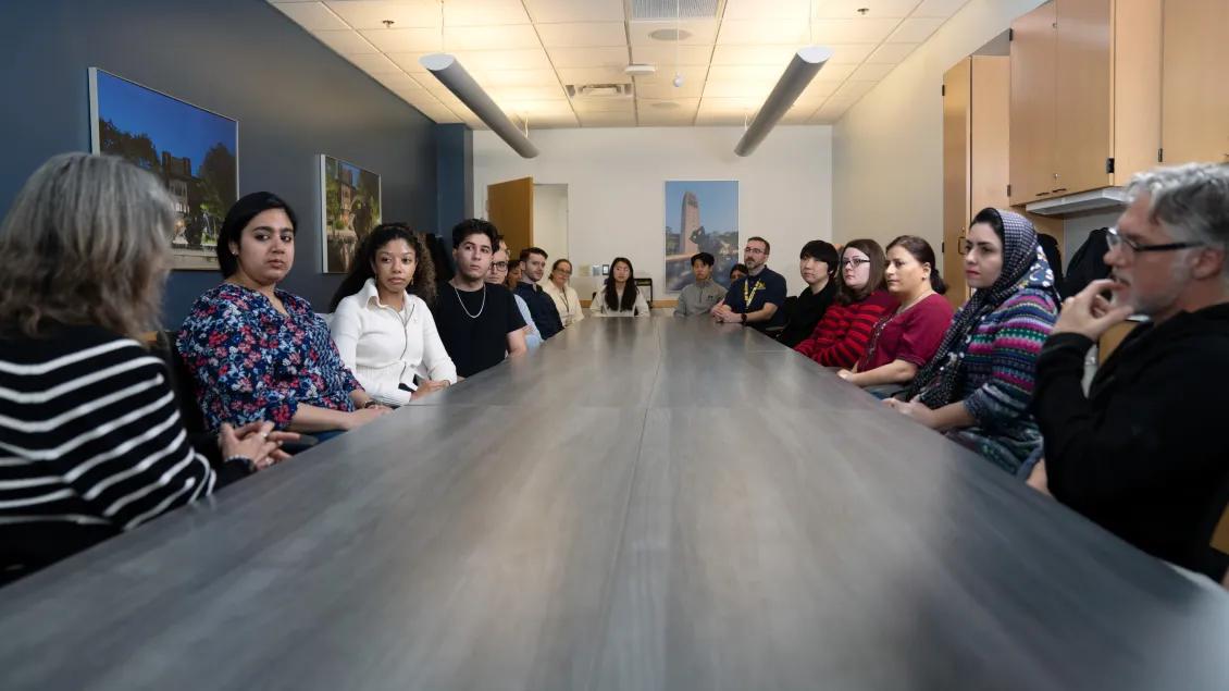 Group of people seated around conference table listening to a speaker at the head of the table