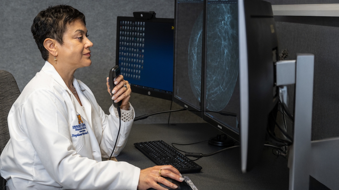 Radiologist reviewing breast imaging scans on dual monitors while speaking into a dictation microphone