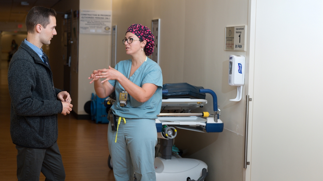 Female provider in scrubs speaks to man in hospital hallway