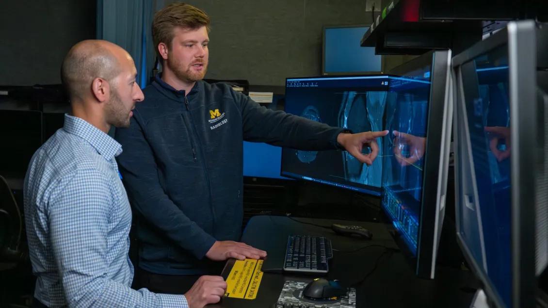 Two male Radiologists point to a scan at a computer