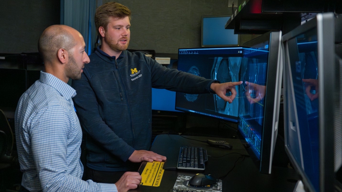 Two male Radiologists point to a scan at a computer