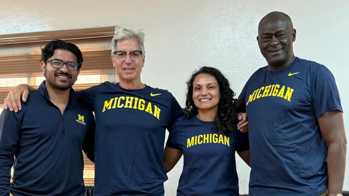 Four clinicians in matching ‘Michigan’ shirts stand arm-in-arm, smiling, during a global health collaboration visit