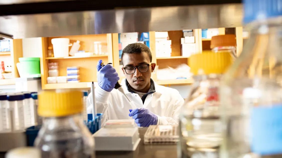 Researcher pipetting in the center, surrounded by vials in the foreground
