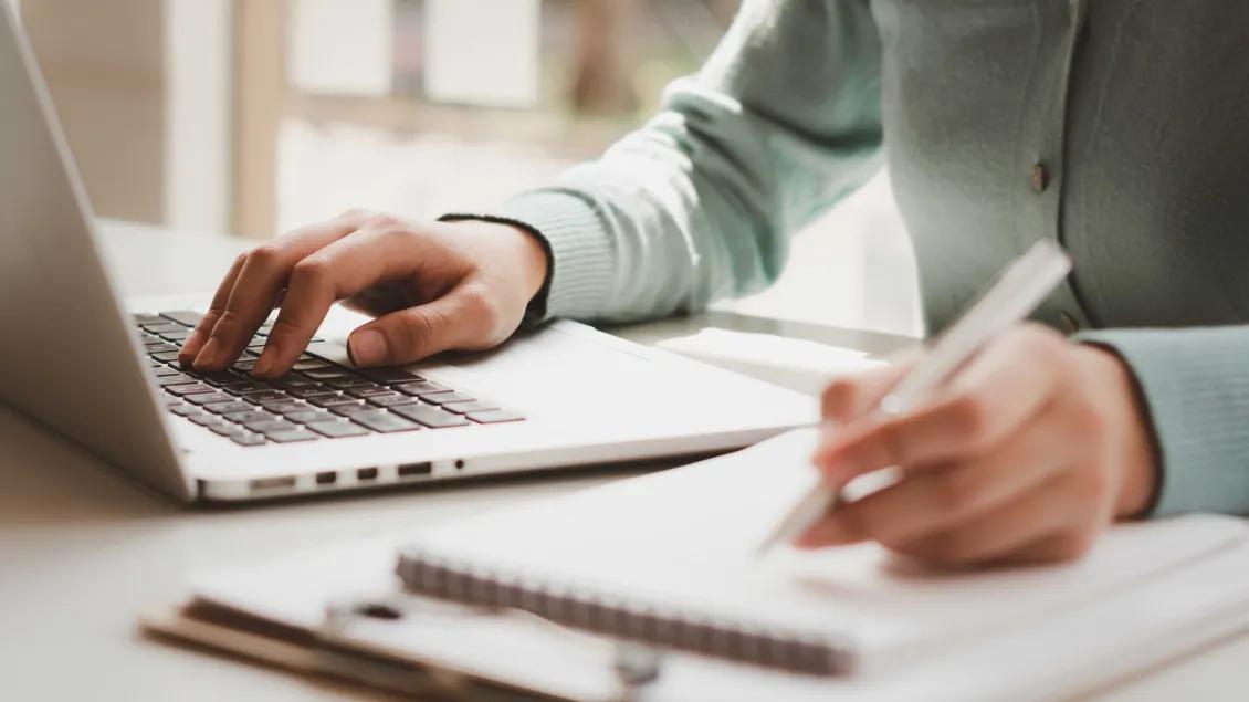 Person using a laptop and writing in a notebook