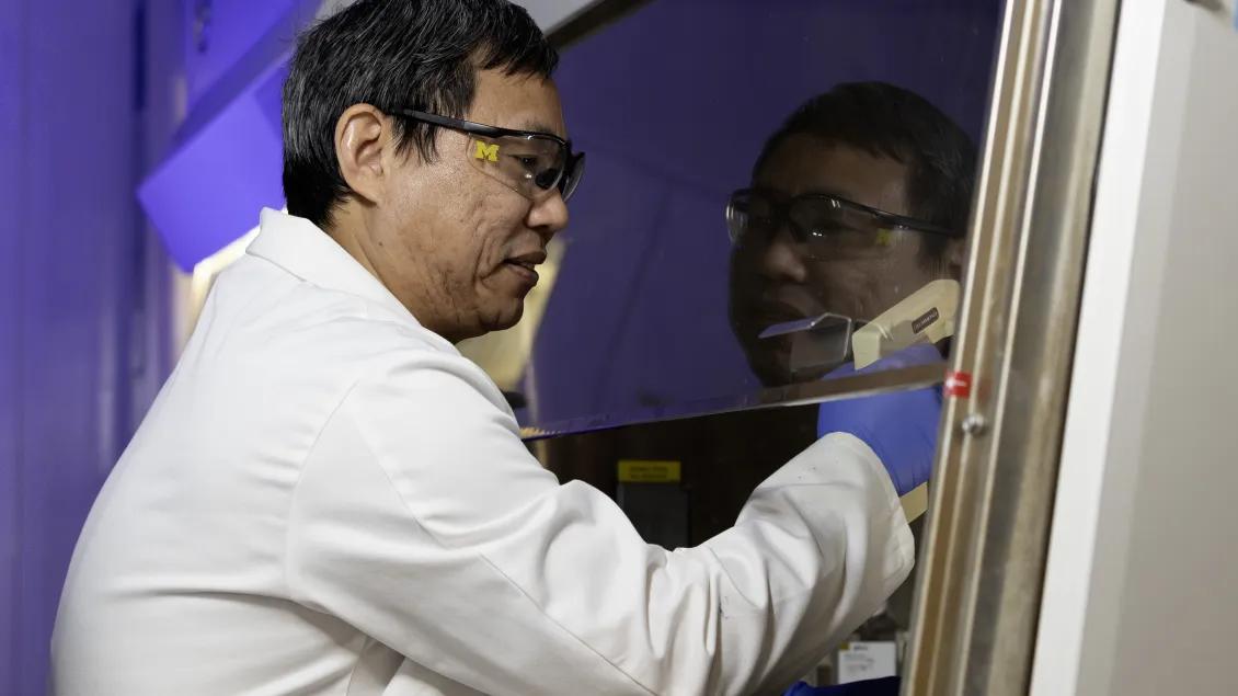 A scientist in a lab coat works with focused intent inside a lab enclosure.
