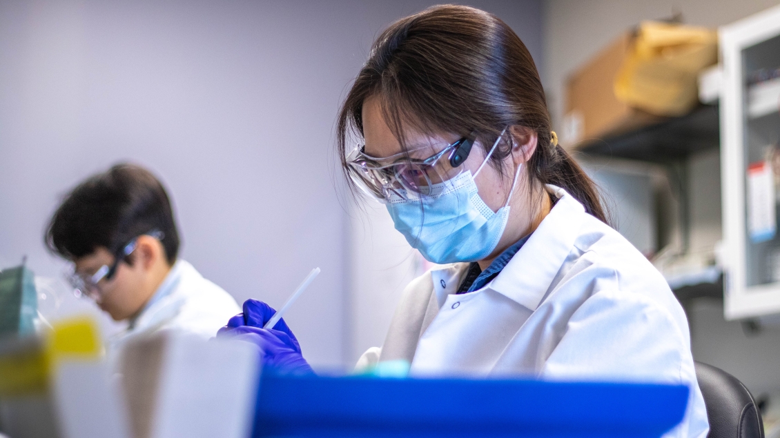 Lab members with white coat and glasses working on a lab.