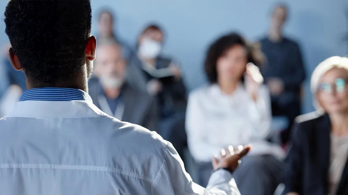 person in white coat speaking to a crowd
