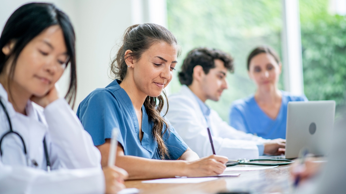 Group of doctors sitting at a table writing on paper and typing on laptop