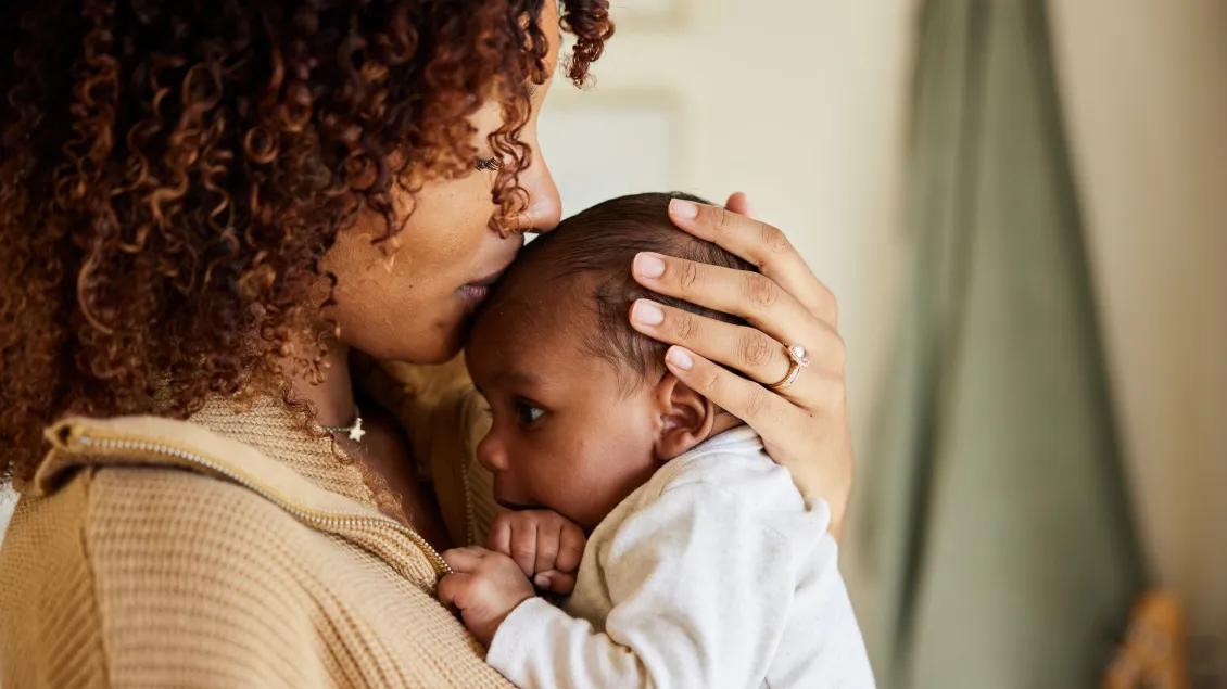 Woman holding baby and kissing baby on the forehead