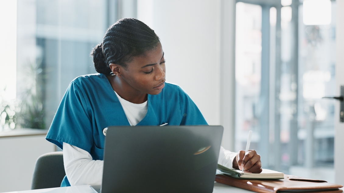 Photo of a woman sitting in front of a laptop taking notes