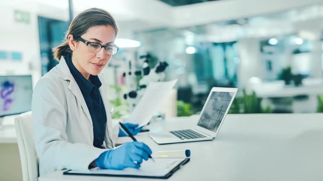 researcher working in a lab using a laptop and a notebook