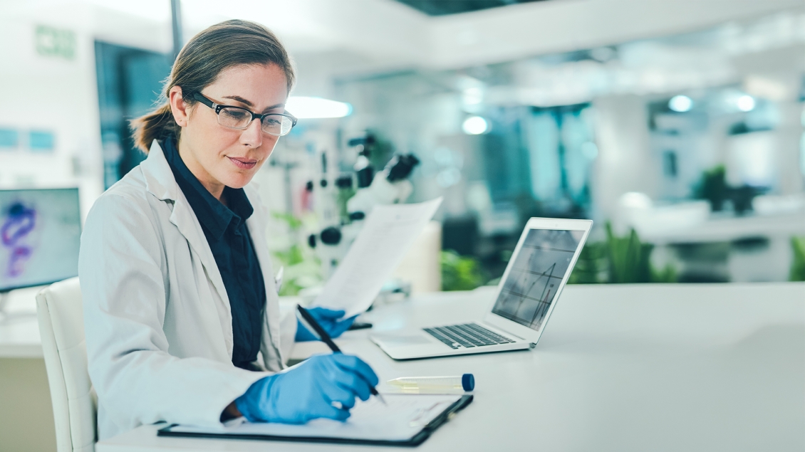 researcher working in a lab using a laptop and a notebook