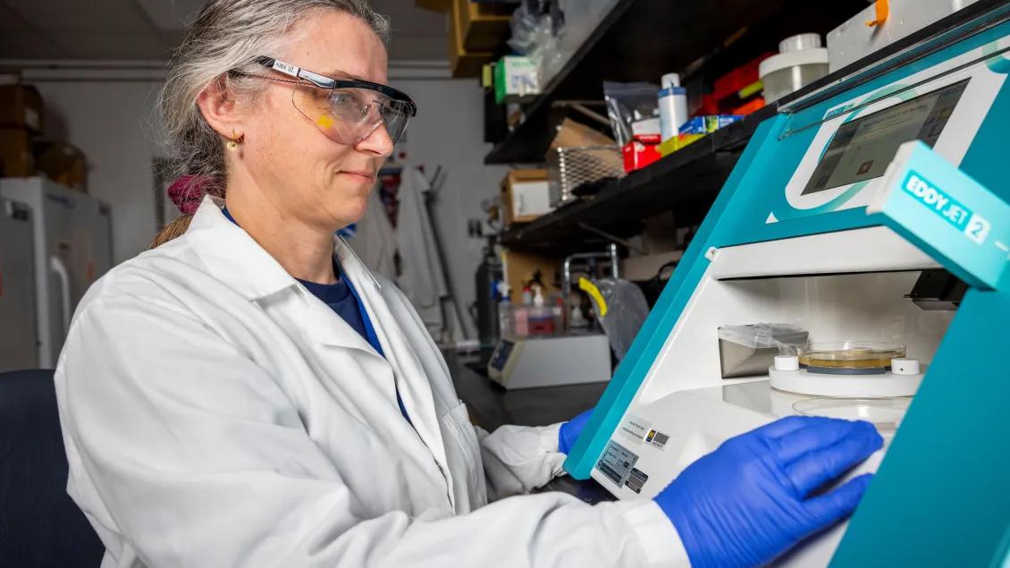 A scientist wearing safety goggles and a lab coat operates a machine in a laboratory.