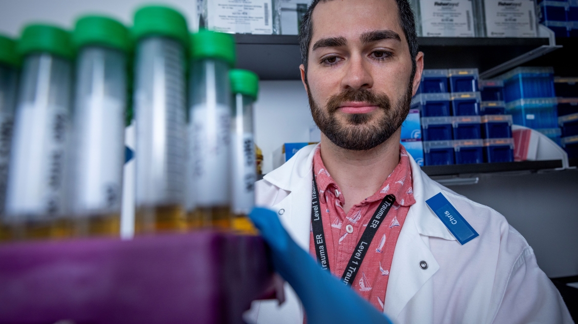 A scientist in a lab coat examines test tubes with green caps held in a rack.