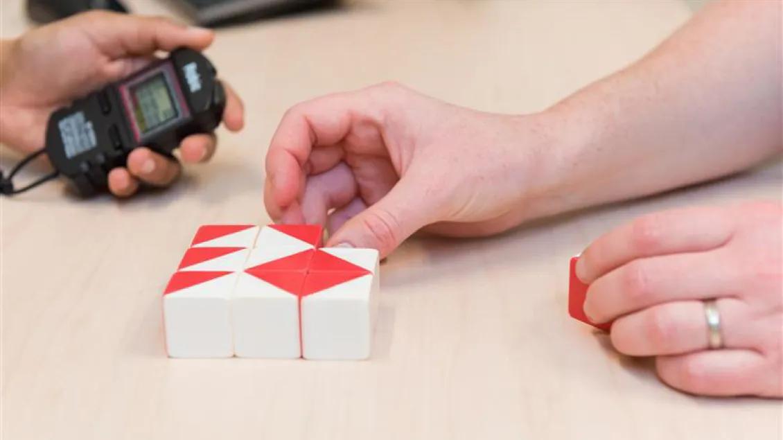 Close up of person holding a stopwatch and someone creating a pattern out of blocks