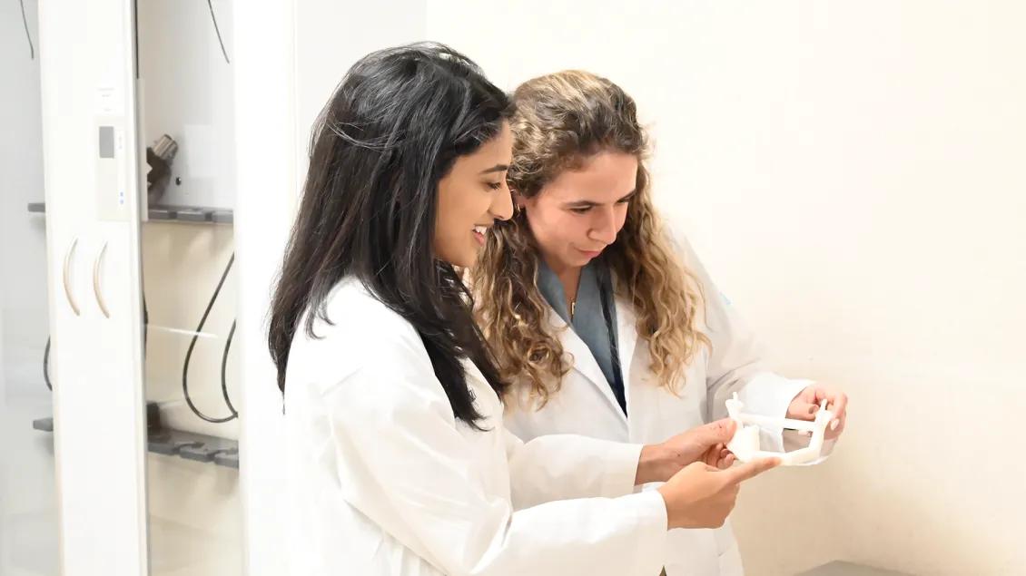 Two people in white lab coats looking at a 3D printed device