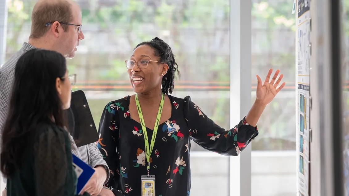 Woman describes her scientific poster to two attendees