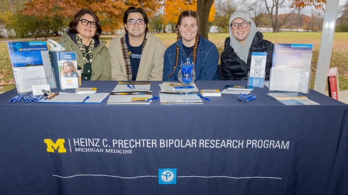 A group of people sit behind a table covered with a navy tablecloth displaying the logo and name of the Heinz C. Prechter Bipolar Research Program at Michigan Medicine.