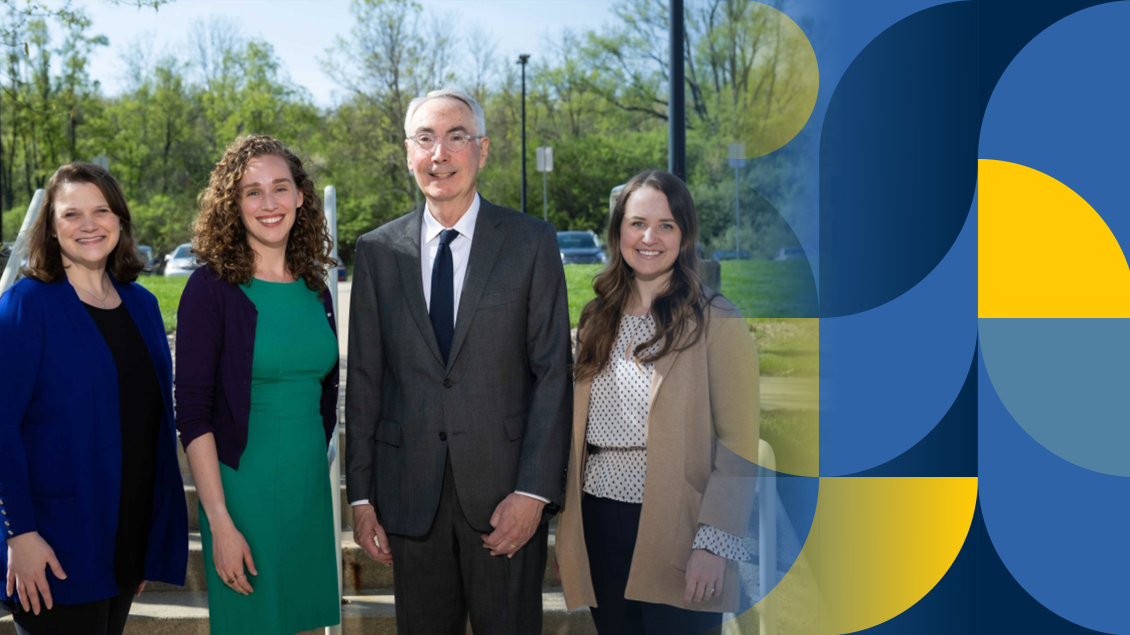 Four faculty members stand together outside on a bright, spring day