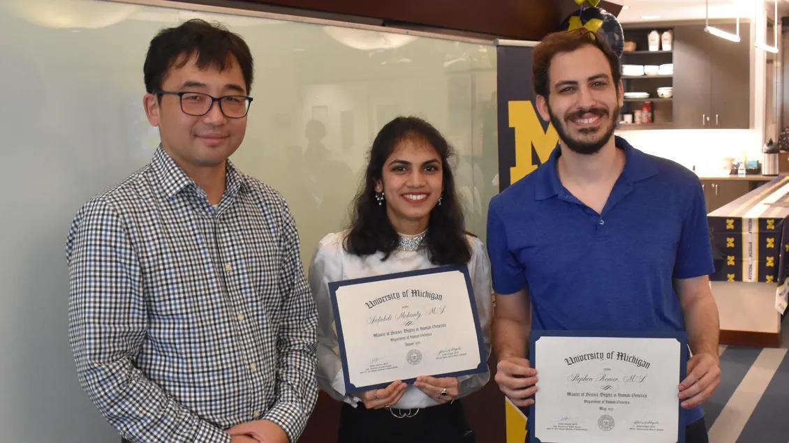 Faculty professor standing with two MS graduate students holding their certificates