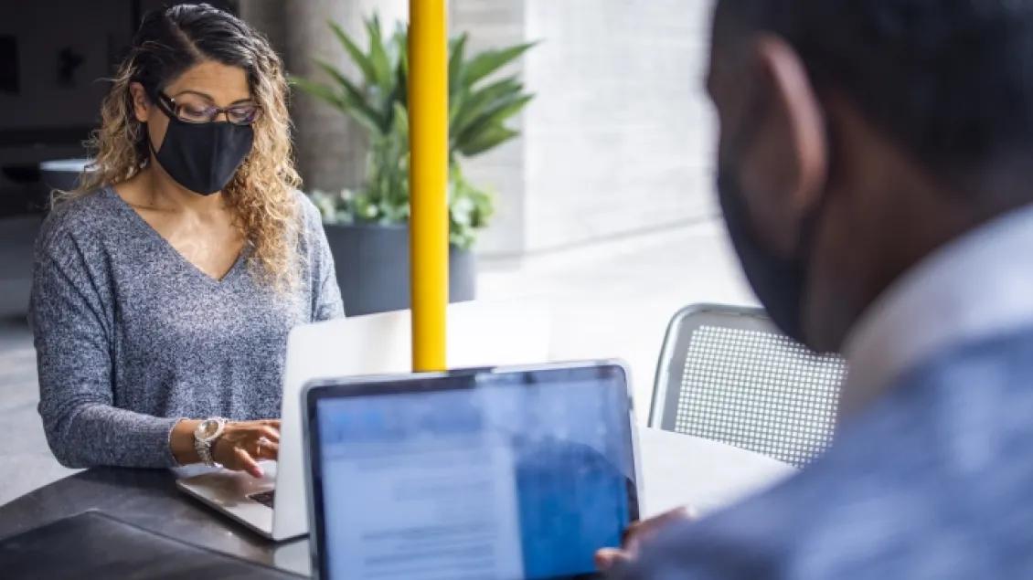 A male and female software engineer face each other while coding on thier laptops