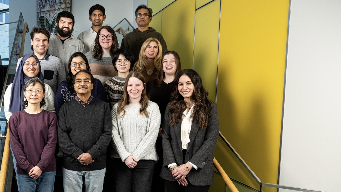 Diverse group of lab team members standing in a group on the stairs with a yellow background