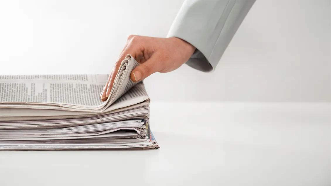 close-up photo of woman's hand grabbing a printed newspaper from a stack