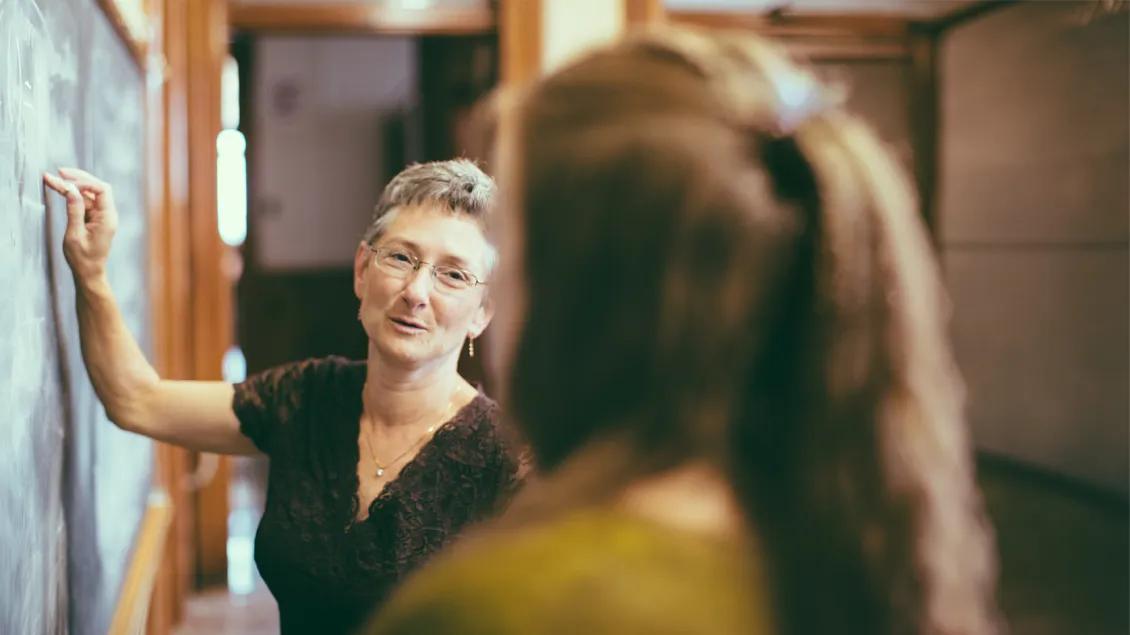 woman writing on a chalkboard and talking to another woman