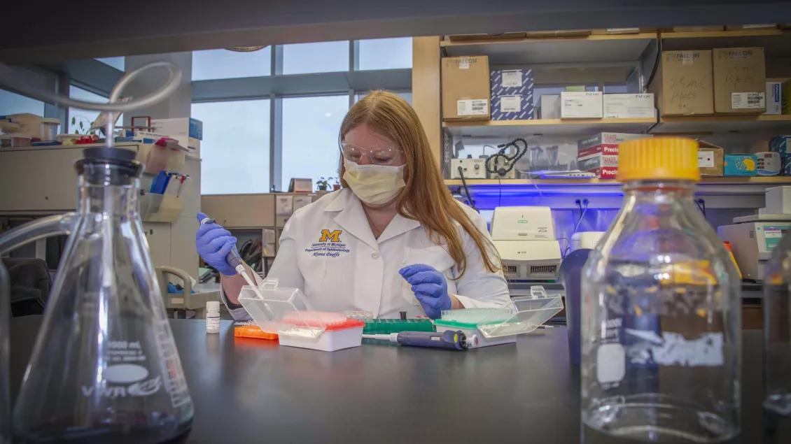 A person wearing a medical mask uses a pipette while working in a lab