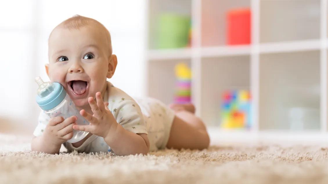 happy baby with a bottle playing on the floor