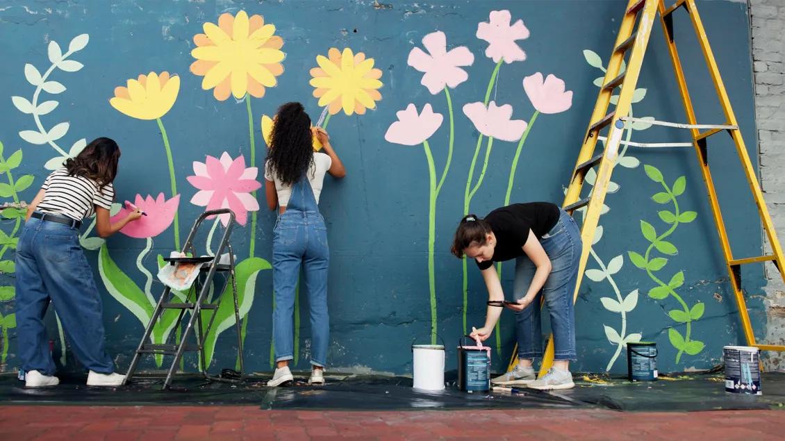 young adults painting a floral mural on an exterior building