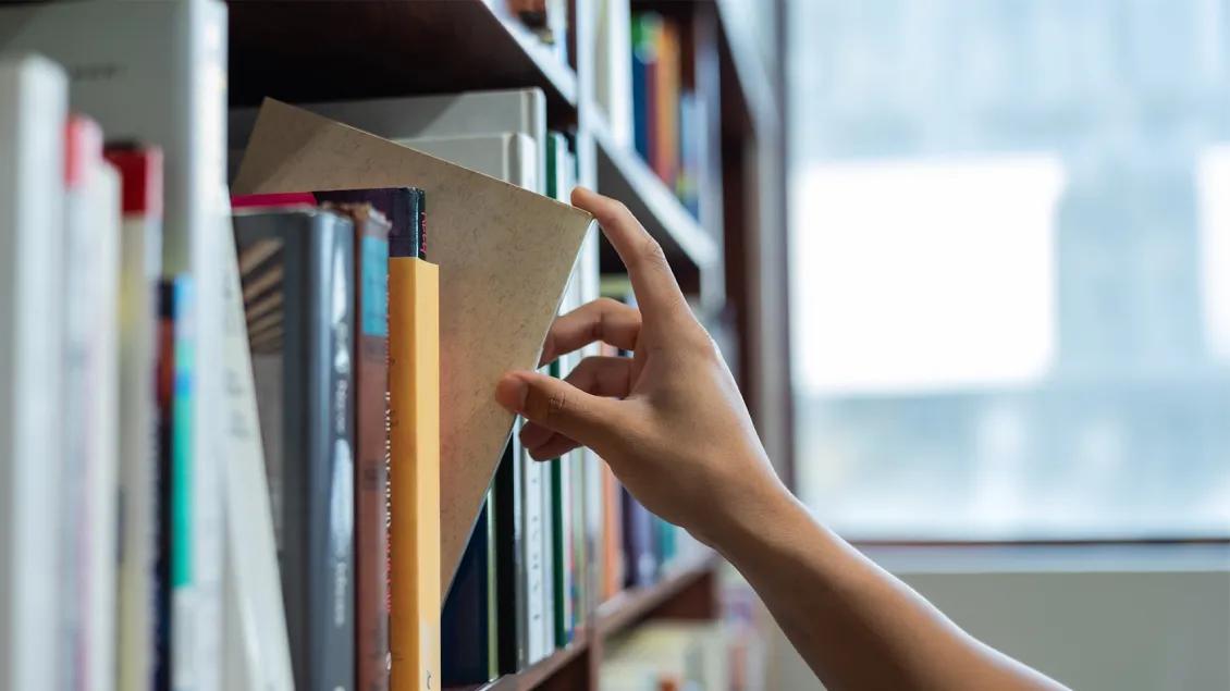 hand reaching for a book from a large book shelf