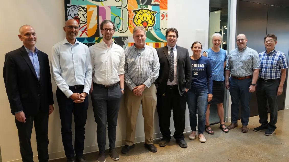 Photo showing nine members of the MNI Executive Committee gathered and posing in a group against a beige wall with a colorful painting in the background