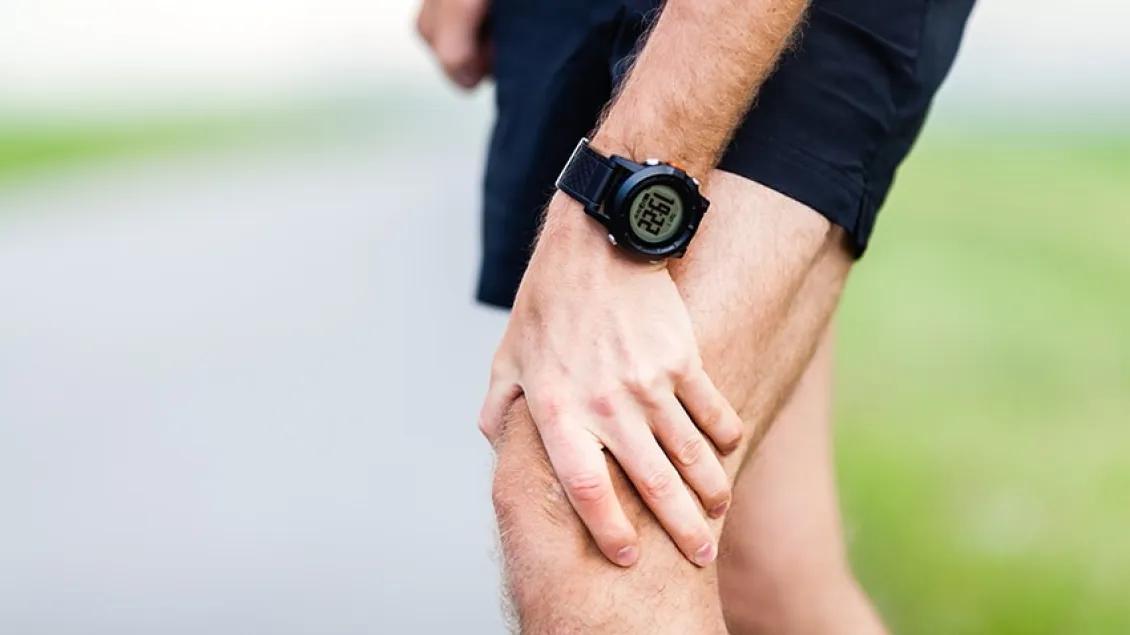 A person wearing a black digital watch holds their knee