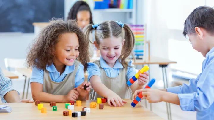 Children playing blocks at school desk.
