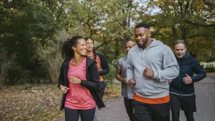 group of multicultural men and women running and smiling on a wooded path