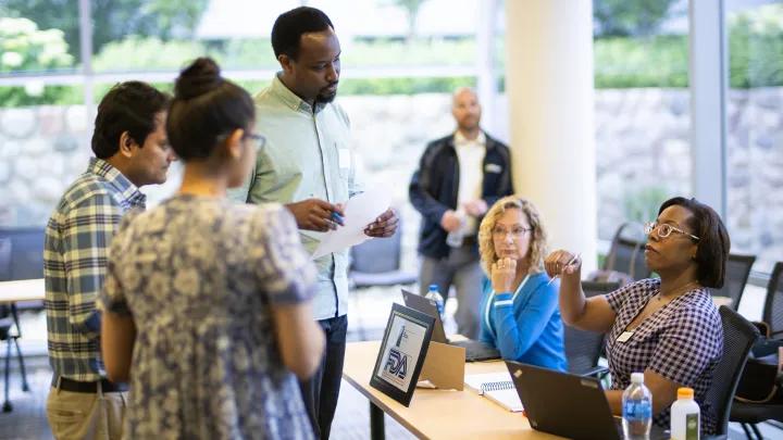 A diverse group of adults engages in a discussion around a table with laptops.