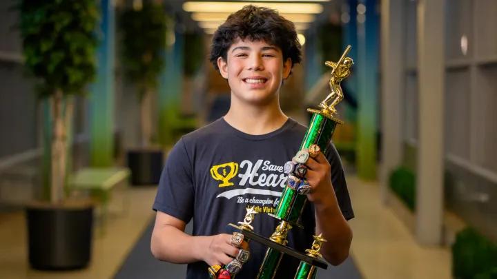 teen boy smiling and posing with green gold trophy blurred background hallway