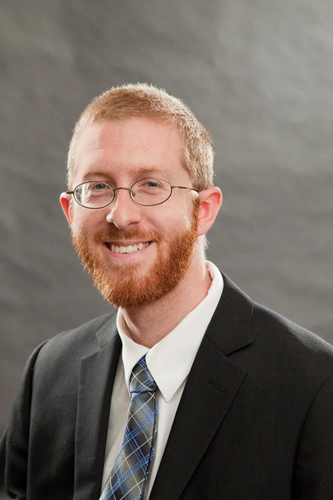 a man with red hair and glasses wearing a white button up shirt and tie 
